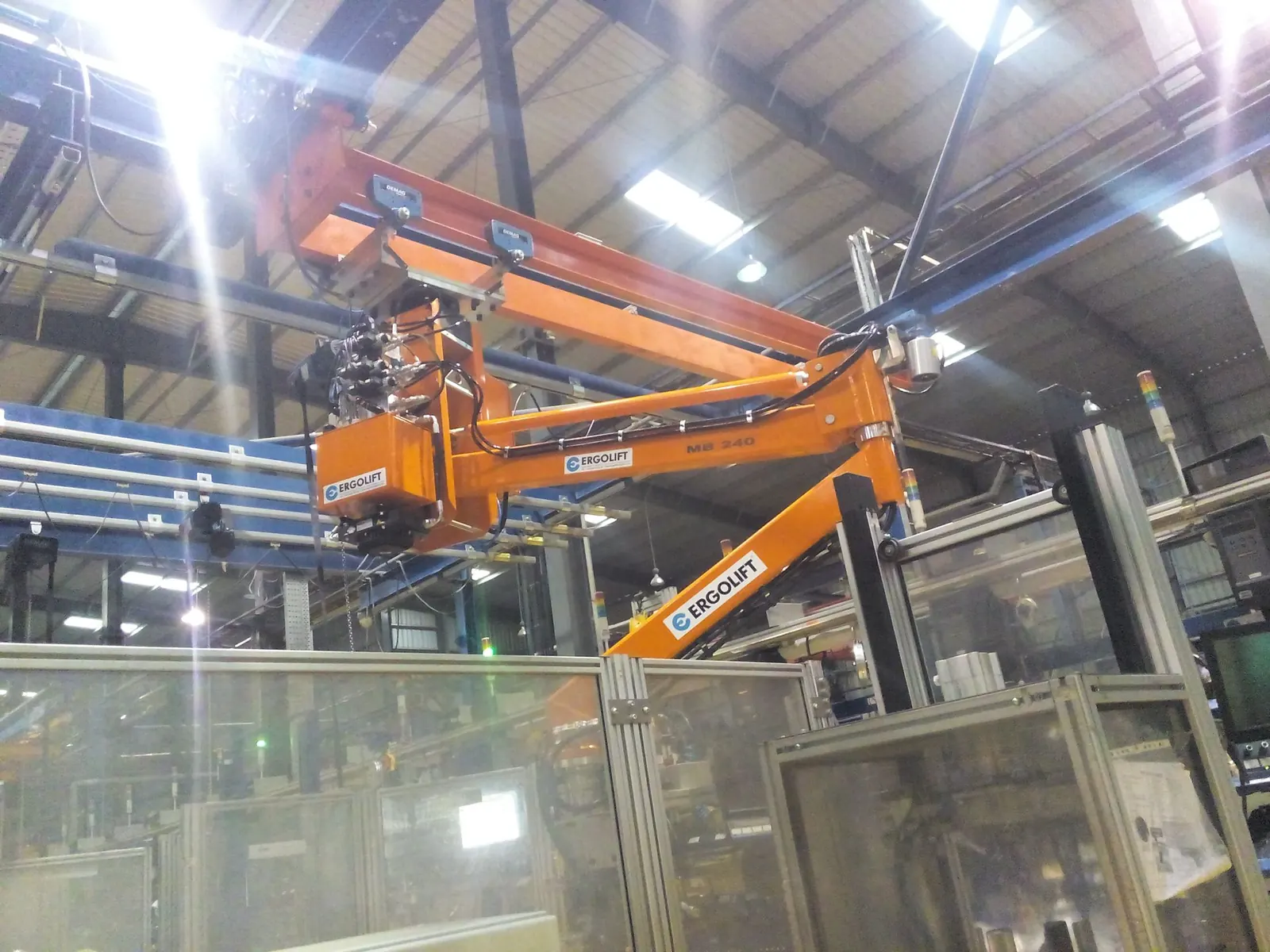 Orange Ergolift manipulator mounted above a guarded assembly cell