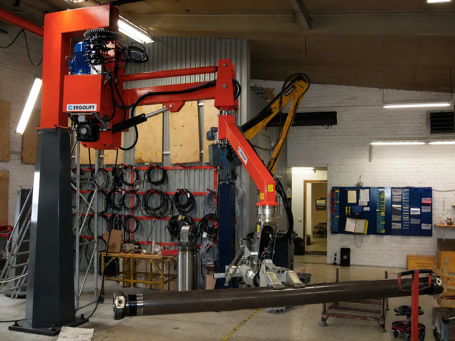Red Ergolift pneumatic manipulator lifting a long steel shaft in a workshop