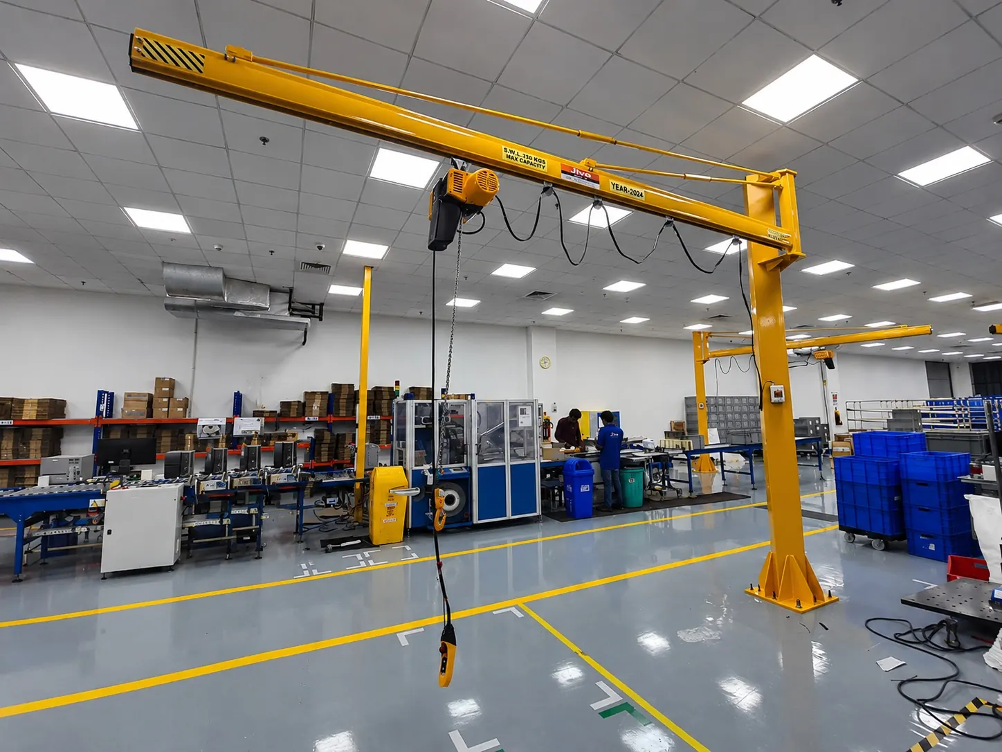 Yellow pillar-mounted jib crane with an electric chain hoist on a clean shop floor