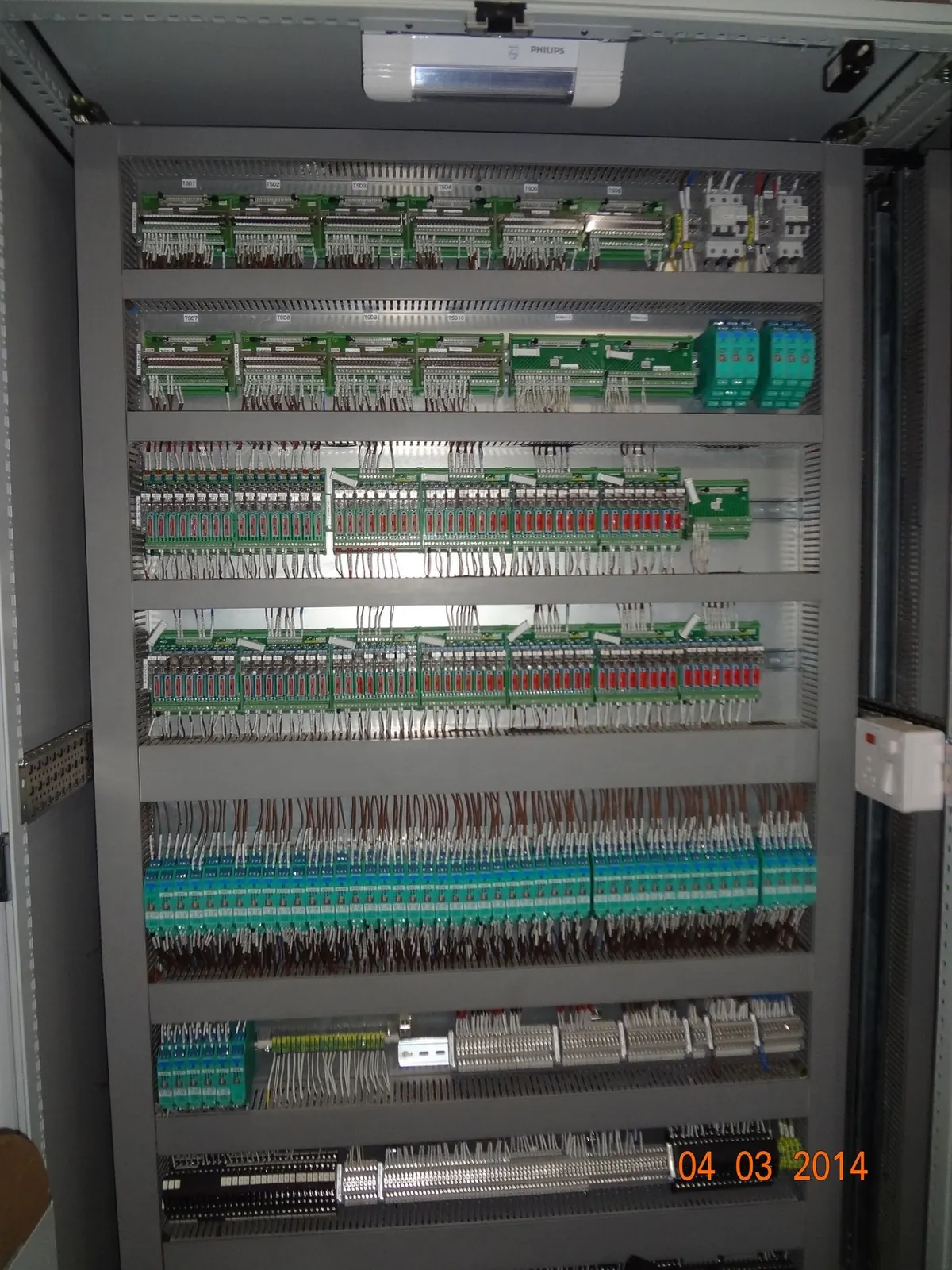 Open control cabinet with rows of neatly wired PLC I/O modules and relays