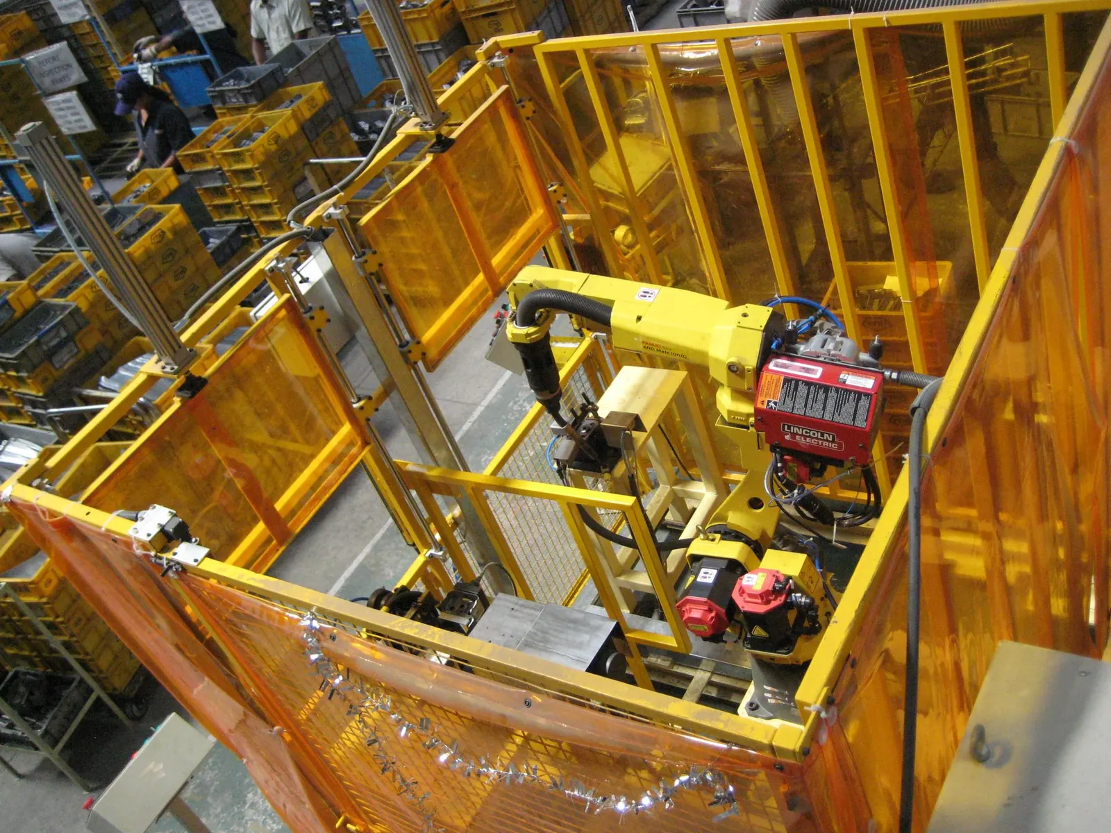 Yellow industrial robot inside a guarded welding cell with amber safety screens