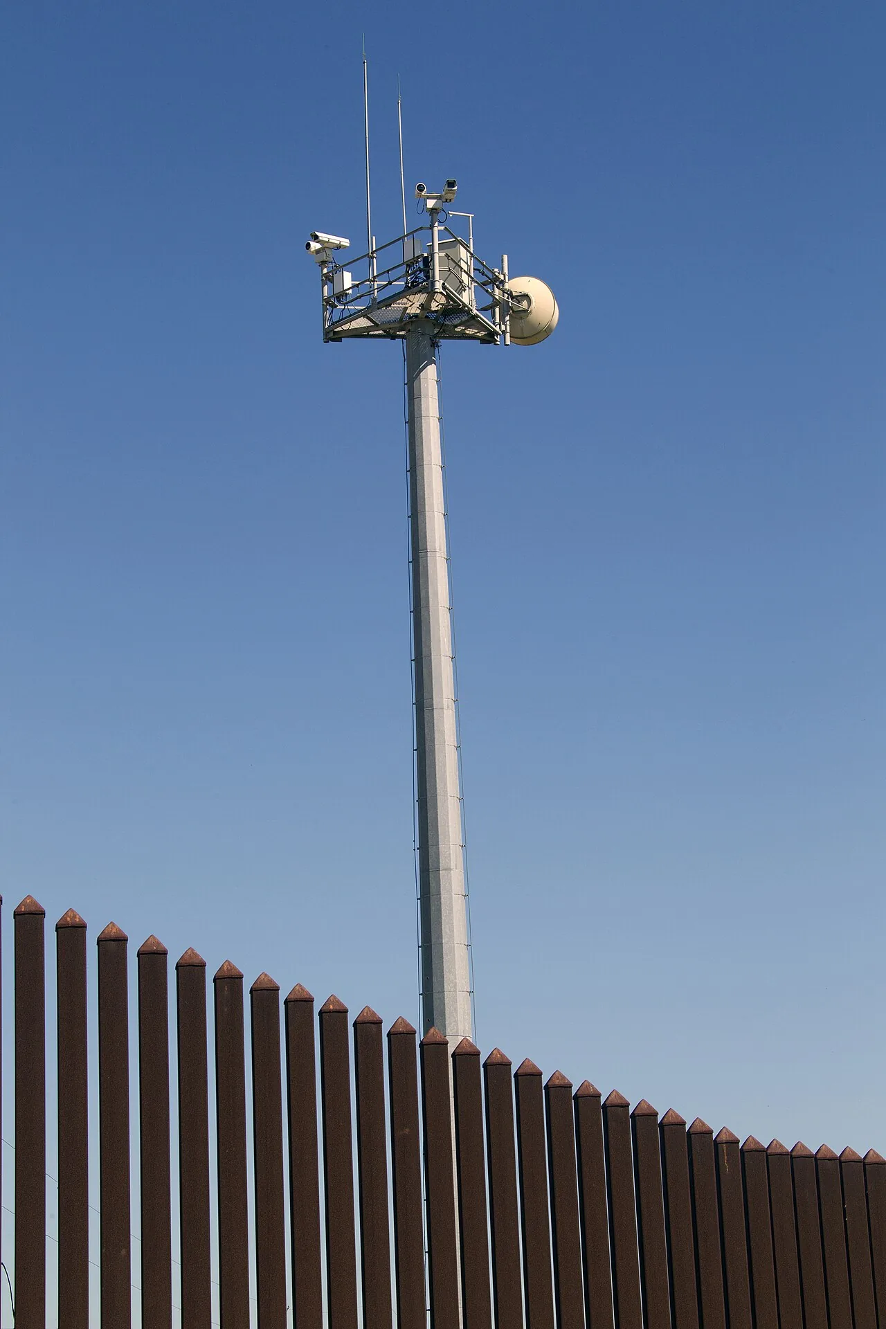 Camera mast beside a tall steel perimeter fence