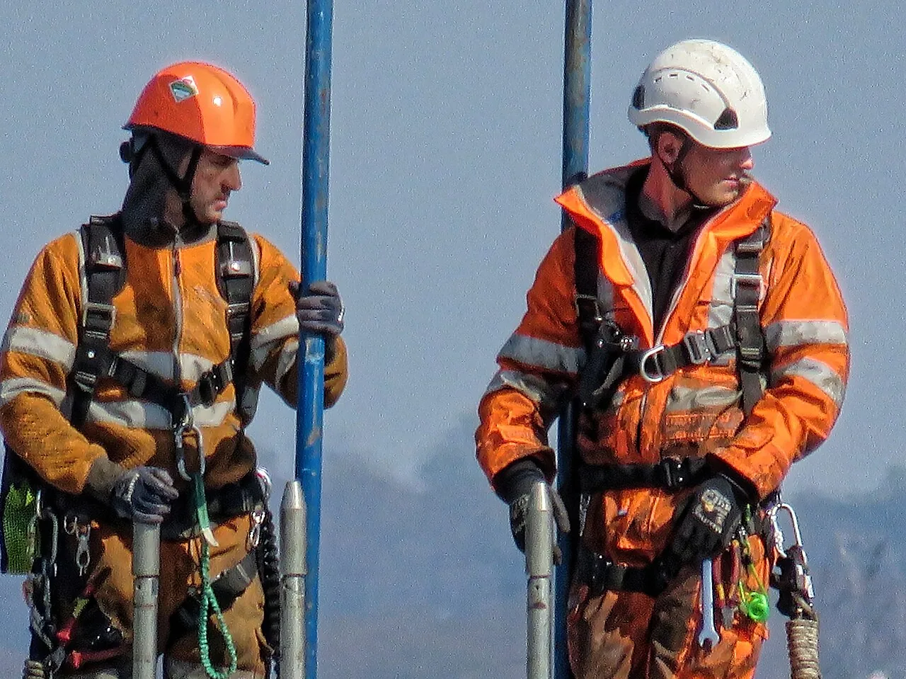 Two workers in hard hats, high-visibility suits and safety harnesses